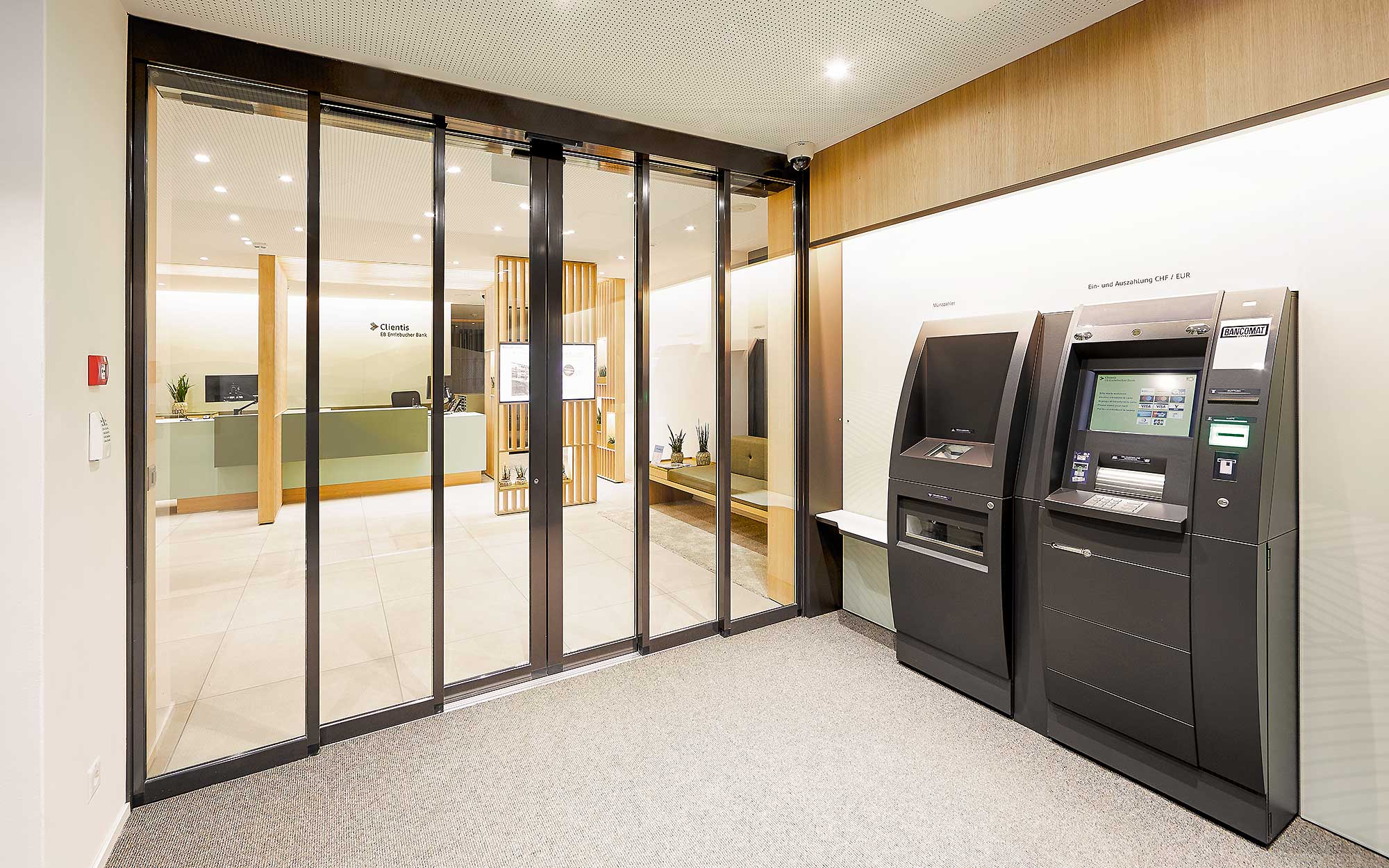 24-Stunden-Zone mit zwei Bancomaten vor der automatischen Schiebetüre der Bank.