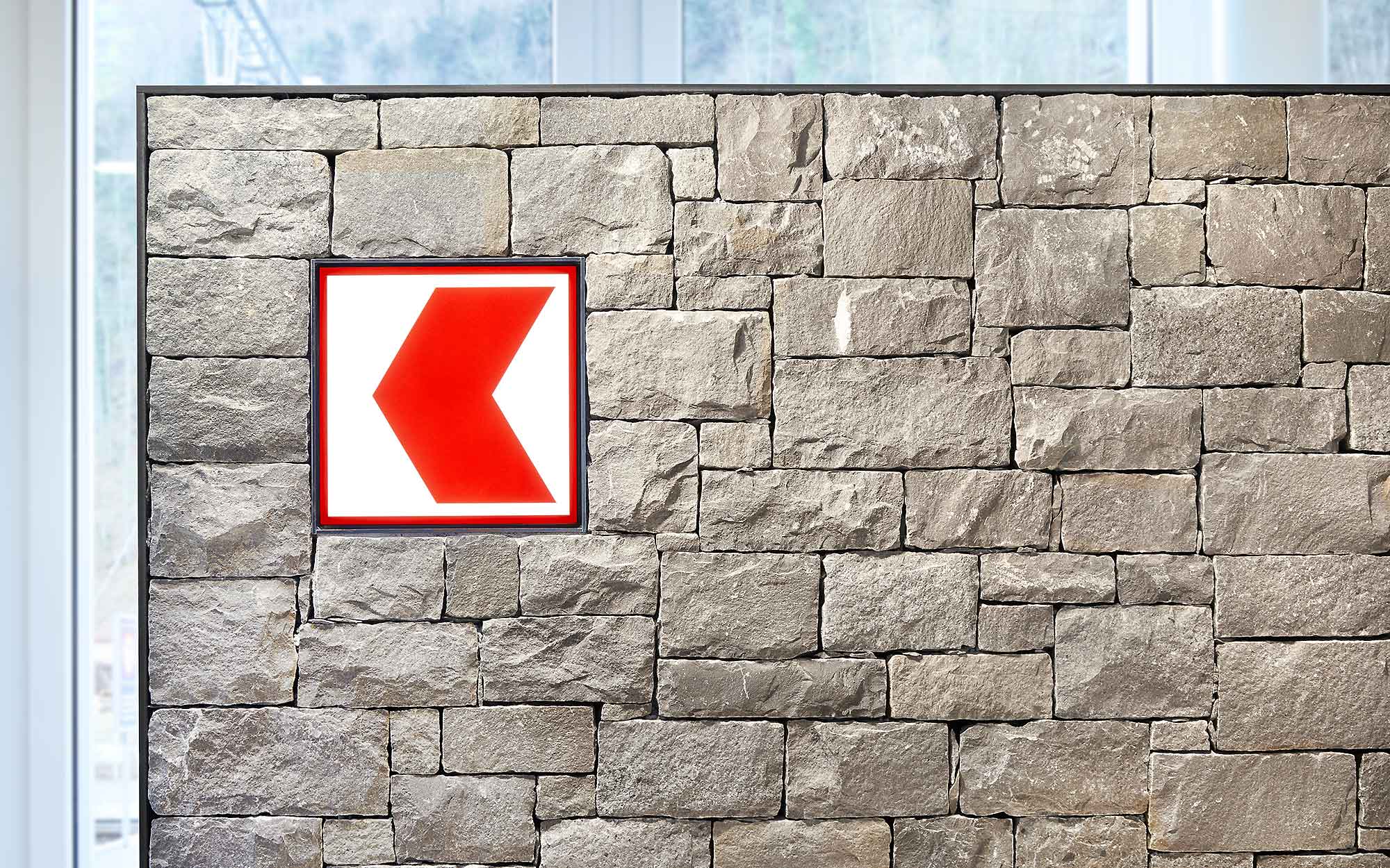 Graue Trockensteinmauer aus Guber Granit mit rotem Banklogo