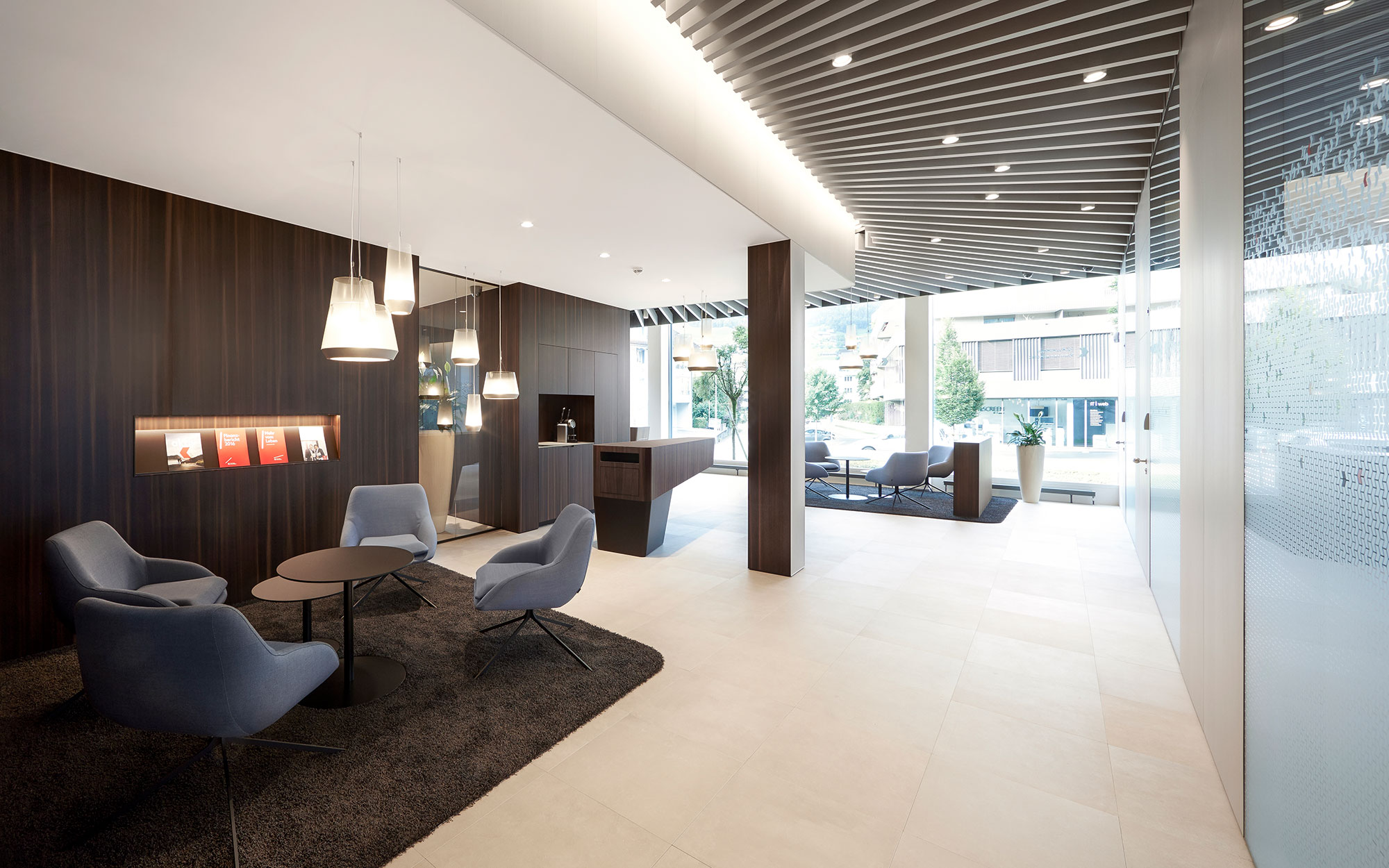 Kundenlounge mit dunklen Einzelsesseln auf dunklem Teppich. Edles Beleuchtungskonzept.