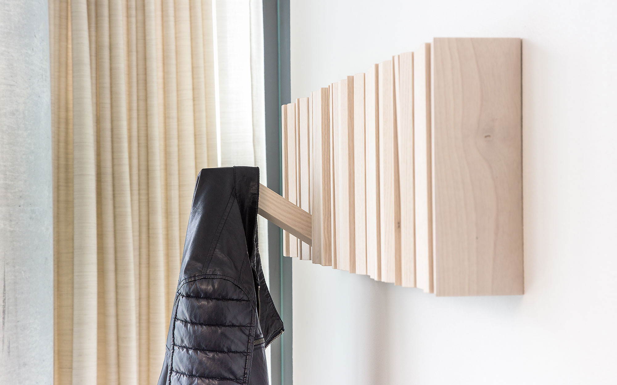 Schwarze Jacke hängt an Eichenlamellen, die horizontal an der weissen Wand angebracht sind